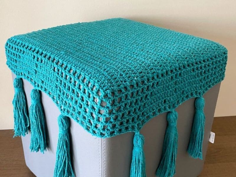 Puff cinza com uma moderna capa de crochê turquesa com detalhes em franjas.