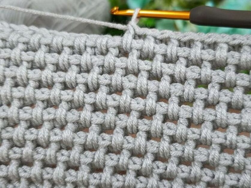 Close-up de um trabalho de crochê cinza, mostrando um ponto de crochê criativo e texturizado.