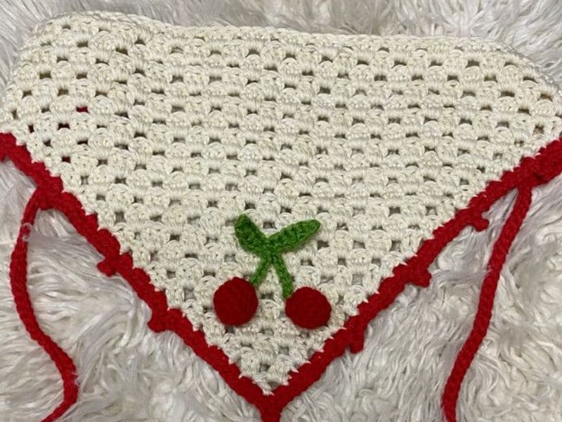 Bandana de crochê branca com detalhes e aplicações de cereja em vermelho e verde.