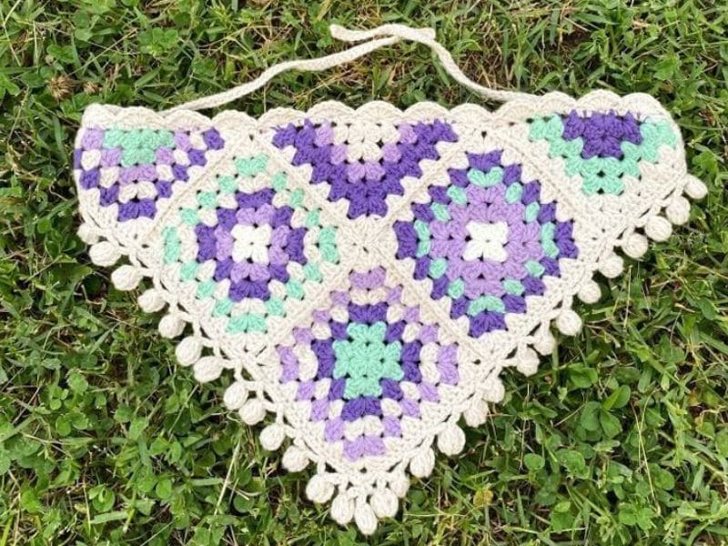 Bandana de crochê com quadrados roxos e verdes sobre a grama.
