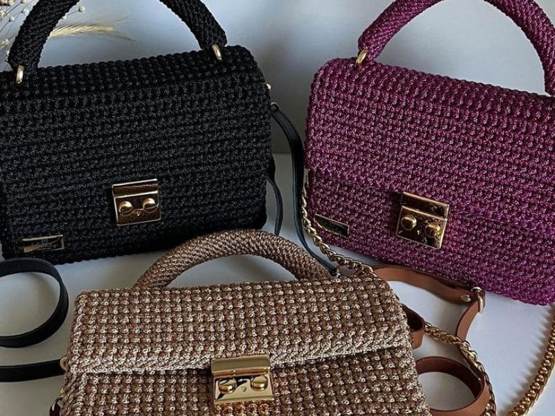 Três bolsas de crochê de luxo em preto, roxo e dourado, com detalhes em metal dourado.