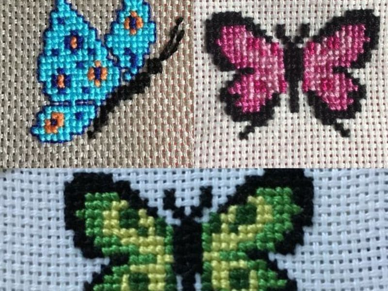 Detalhe de três borboletinhas coloridas bordadas em ponto cruz.