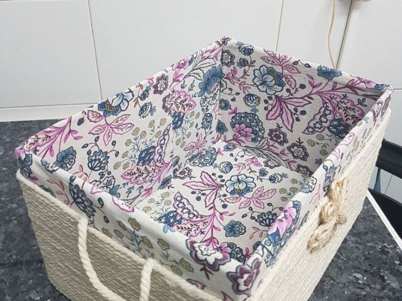 Caixa organizadora de papelão revestida com tecido floral em tons de rosa, azul e branco.