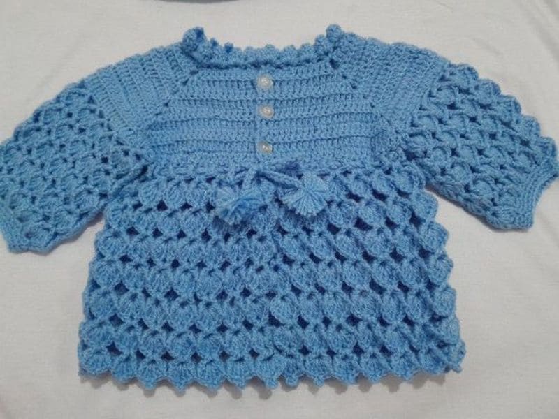 Casaco de bebê em crochê azul claro, com padrão texturizado e detalhes de botões.