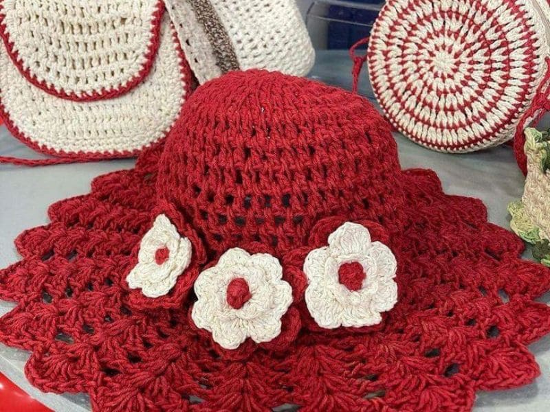 Chapéu de praia bucket em crochê vermelho com detalhes de flores brancas.