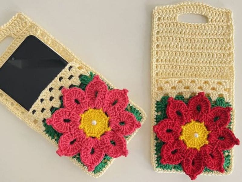 Dois suportes de celular de crochê bege com flores rosa e detalhes em verde e amarelo.