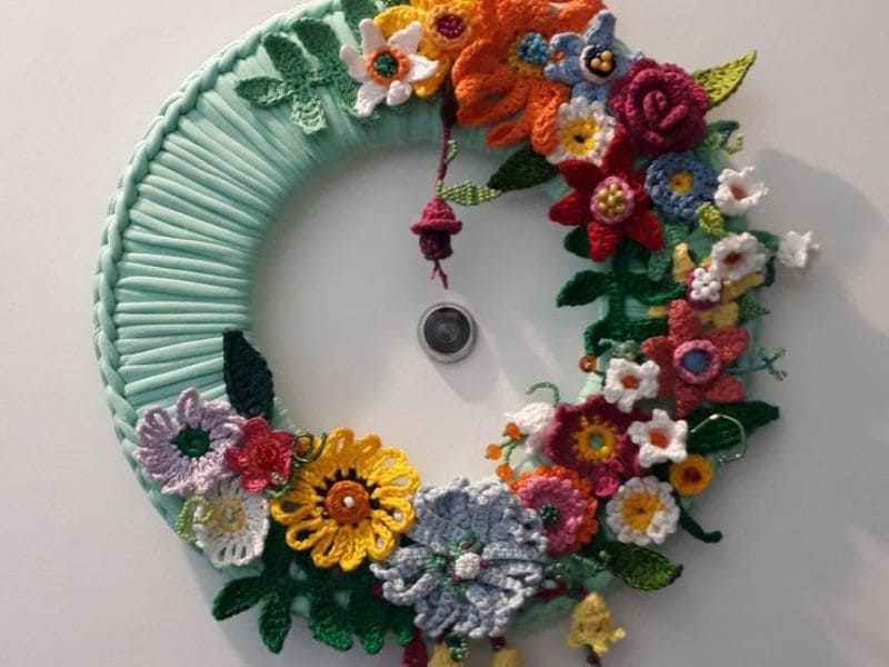 Guirlanda decorativa de crochê com flores coloridas, pendurada em uma porta branca.