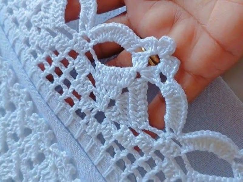 Detalhe de um novo bico de crochê branco sendo segurado por uma mão.